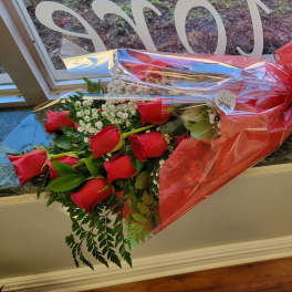Wrapped bouquet of red roses and white filler flowers in red cellophane with a large bow