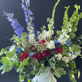 Large bouquet of red and white roses with blue delphinium in a white vase