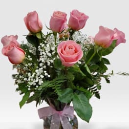 Glass vase of pink roses with white filler flowers and a pink ribbon bow