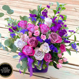 Mixed bouquet of pink and lavender roses with purple flowers in a purple vase