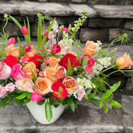 Low centerpiece of peach, pink, and red roses with tulips in a white vase