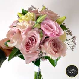 Hand-tied bouquet of pale pink roses and cream blooms held against a light background