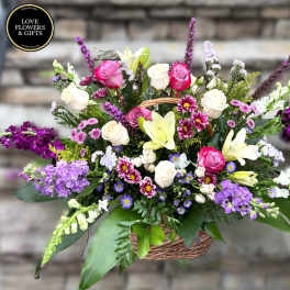 Large mixed basket arrangement with pink and white roses, lilies, and purple accent flowers.