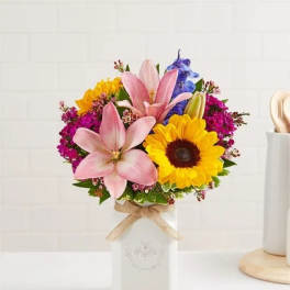 Bouquet of pink lilies, sunflowers, and purple flowers in a white vase