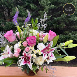 Pink roses and white lilies with accent blooms arranged in a low glass vase