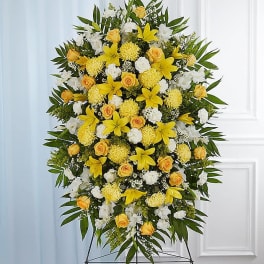 Tall standing spray of yellow lilies, yellow roses, and white flowers on an easel