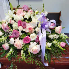 Pink, lavender, and white rose and lily casket spray with a lavender ribbon.