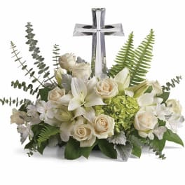 Low arrangement of white lilies and roses with green hydrangea and a clear crystal cross in the center