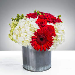 Red roses and gerbera daisies in a ribbed metal container with white hydrangeas