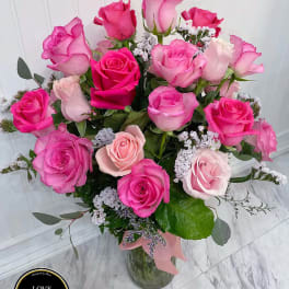 Tall glass vase of hot pink and light pink roses with white filler flowers and a pink ribbon