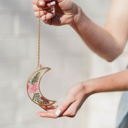 Hands holding a crescent moon ornament with pressed flowers