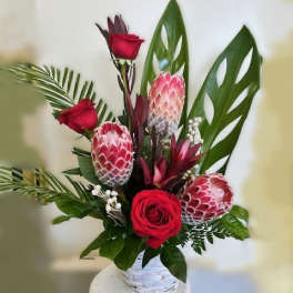 Red roses and pink protea in a white basket vase