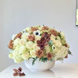 Cream and peach floral arrangement in a white bowl vase with burgundy orchids