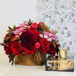 Red roses and pink orchids in a gold box with a candle beside it