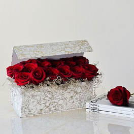 Box of red roses with one rose beside a stack of Chanel books