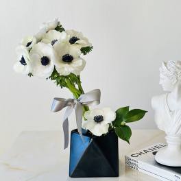 White anemone bouquet in a black vase with a silver ribbon
