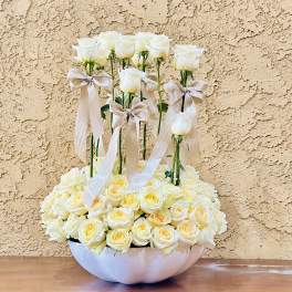 White roses arranged in a low bowl with tall rose stems and satin bows