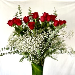 Red roses in a tall glass vase with baby's breath and eucalyptus