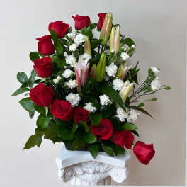 Red roses and white lilies arranged in a vase with small white filler flowers