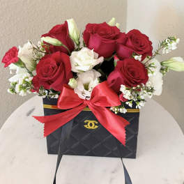 Red and white roses arranged in a black gift box with a red bow