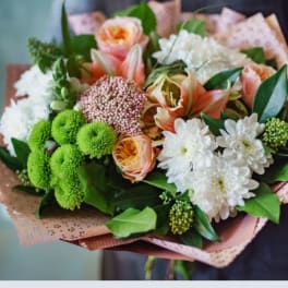 Handheld bouquet of peach and white flowers with green accents