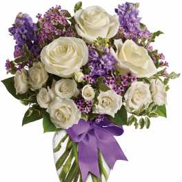 White roses and purple flowers arranged in a glass vase with a purple ribbon.