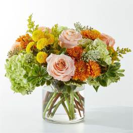 Bouquet of peach roses, yellow mums, and green hydrangeas in a glass vase