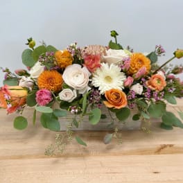 Low rectangular flower arrangement with orange, white, and pink blooms in a wooden box