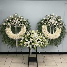 Three white floral funeral wreaths and sprays on stands