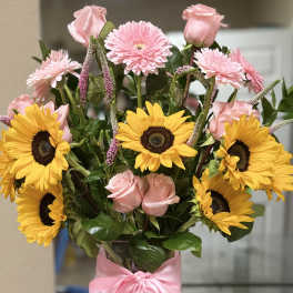 Bouquet of pink roses and yellow sunflowers in a clear vase with a pink ribbon