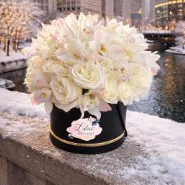 White roses and pale orchids in a black hatbox