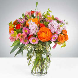 Mixed bouquet of orange, pink, and red flowers in a clear glass vase