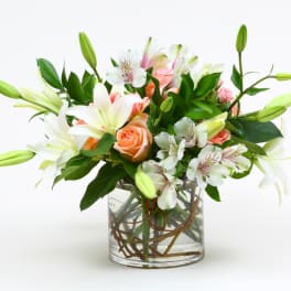 Bouquet of white lilies, peach roses, and white alstroemeria in a glass vase