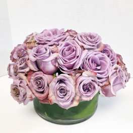 Lavender roses arranged in a low green glass vase