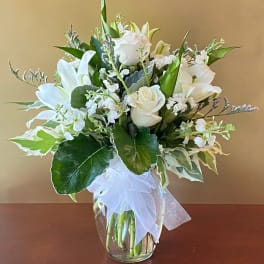 White lilies and roses in a glass vase with a white bow
