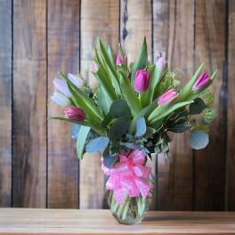 Pink and white tulips in a glass vase with a pink ribbon