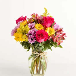 Bright mixed bouquet of pink roses, yellow and purple daisies in a clear glass vase with twine bow