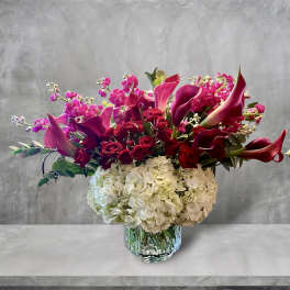 Bouquet of pink calla lilies, red roses, and white hydrangeas in a glass vase
