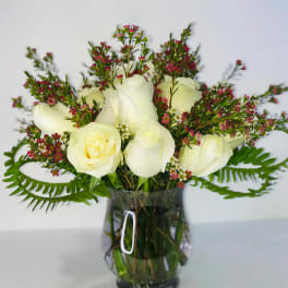 White roses and pink filler flowers arranged in a glass vase
