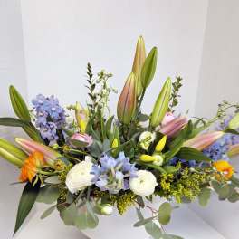Mixed bouquet with lilies, blue flowers, and white blooms in a white vase