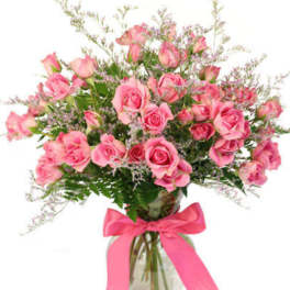 Arrangement of pink roses and filler flowers in a clear glass vase with a pink ribbon bow