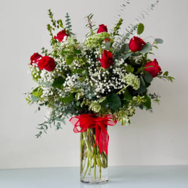 Red roses and white baby's breath in a clear glass vase with a red ribbon