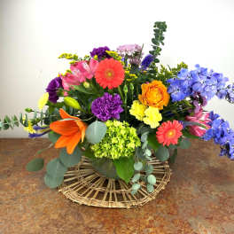 Colorful mixed bouquet in a low vase with orange, blue, pink, and purple blooms
