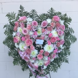 Heart-shaped pink and white floral wreath on a stand with ribbon