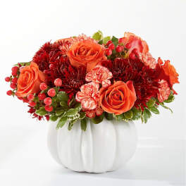 Orange roses and red chrysanthemums in a white pumpkin vase