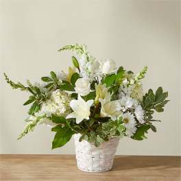 White floral arrangement in a woven basket with lilies and daisies