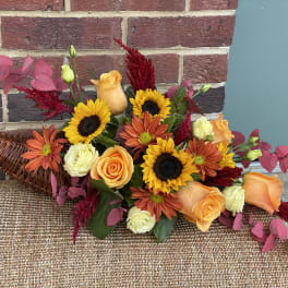Orange roses and sunflowers in a wicker basket with pink foliage