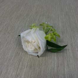 White rose boutonniere with green accents on a fabric surface