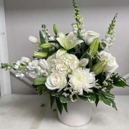 White floral arrangement in a round white vase with lilies and roses
