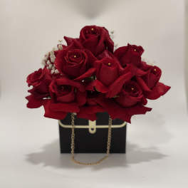 Red rose arrangement in a black gift box with a gold chain handle